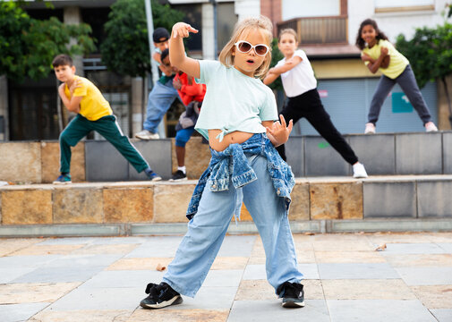 Cute blonde preteen b-girl dancing with group of friends on city street. Urban lifestyle. Hip-hop generation