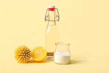 Bottle of vinegar, baking soda, brush and lemon on color background