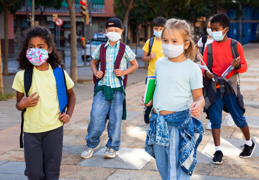 Portrait of preteen schoolchildren in face masks with rucksacks and workbooks on their way to college in warm autumn day. Back to school after lockdown concept