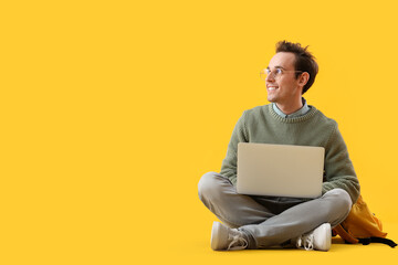 Male student with laptop on yellow background