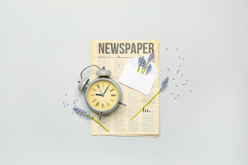 Composition with beautiful Muscari flowers, alarm clock and newspaper on grey background