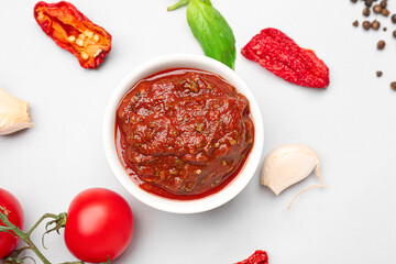 Bowl of delicious tomato sauce and ingredients on grey background