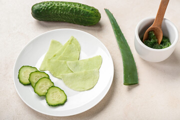 Plate with cotton under-eye patches, cucumber slices and aloe leaf on white background
