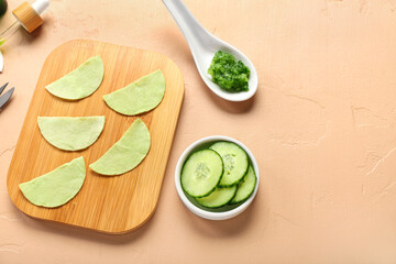 Board with cotton under-eye patches and cucumber slices on beige background