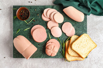 Slate board with tasty boiled sausages and bread on light background