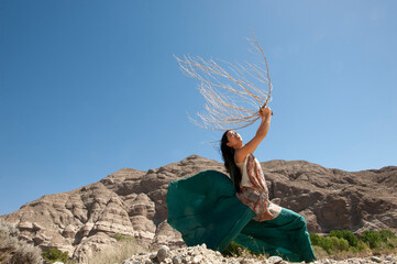 Photography of a beautiful wild woman holding a branch up in the wind.  - 601224982