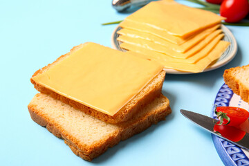 Plates of tasty processed cheese with bread and vegetables on blue background