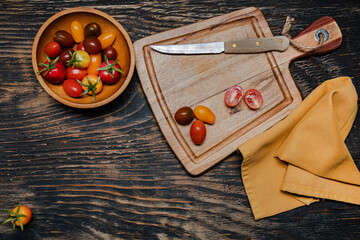 Fototapeta na wymiar ripe cherry tomatoes and knife on cutting board. Dark wooden table. View from above. copy space.