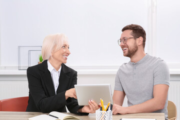 Happy boss with tablet and employee discussing work issues at wooden table in office