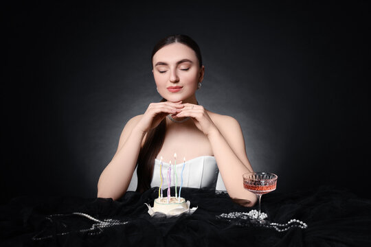 Fashionable photo of attractive young woman making wish with her Birthday cake on black background