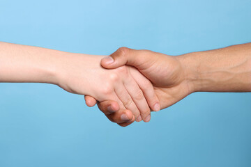 International relationships. People holding hands on light blue background, closeup