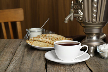 Vintage samovar, cup of hot drink and pancakes served on wooden table. Traditional Russian tea ceremony