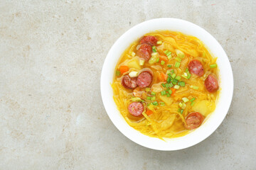 Delicious sauerkraut soup with smoked sausages and green onion on light grey table, top view. Space for text