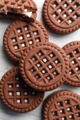 Tasty chocolate sandwich cookies with cream on white wooden table, flat lay