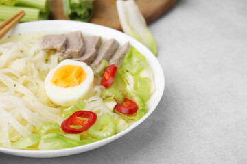 Bowl of delicious rice noodle soup with meat and egg on light grey table, closeup. Space for text