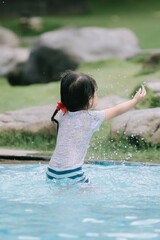 An Asian girl child is splashing water in swimming pool