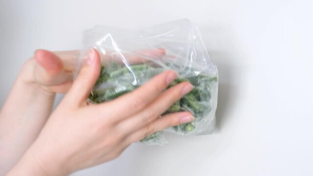 Female hands hold package of frozen string beans on white background.