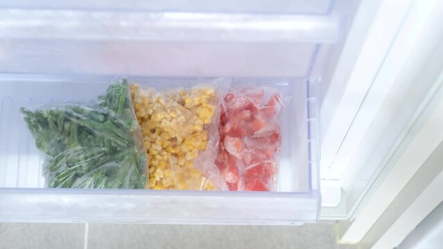Female hand puts plastic bags with vegetables in freezer drawer.