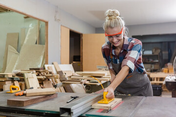 young carpenter woman wear uniform and goggles working use electronic saw cutting wood. craftsman profession in wood factory. woodworking industry.