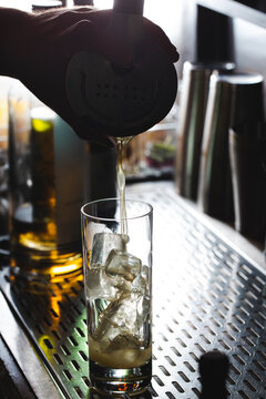 Bartendering pouring out craft cocktail over ice cubes in a tall Collins glass at nightclub