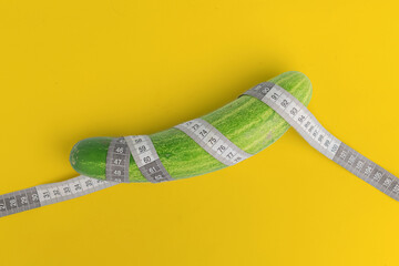 closeup of a cucumber and measurement tape around. concept of penis size measurement isolated on yellow background