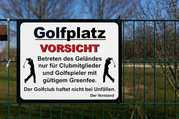  Schild am Zaun eines Golplatzes in Deutschland mit Hinweis auf Unfallgefahr auf dem Gelände
