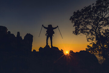 The Man on the mountain. Leadership Concept. Silhouette of hiking man celebrating raising arms on the top of mountain with over sunset or sunrise. Success man on the peak of high rocks