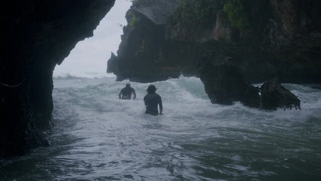 Two persons running through the wild sea to go surving in Bali. Panning shot