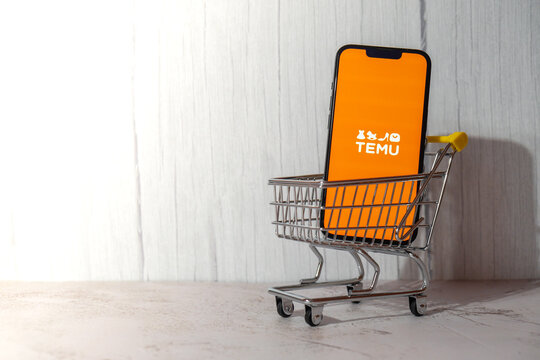 Gdansk, Poland - March 2023 Temu app icon in screen of mobile phone iPhone Apple with shopping cart. Temu subsidiary of China based e-commerce platform Pinduoduo. Online shopping Temu website