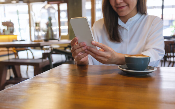 Closeup image of a young woman holding and using mobile phone in cafe