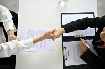 Top view of a recruiter shaking hands with a young male candidate after a job interview. - obrazy, fototapety, plakaty