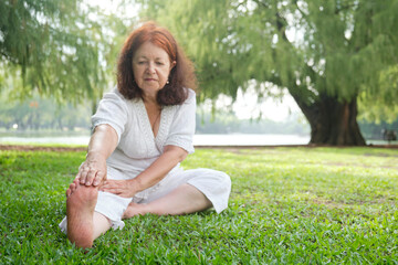 Mature latin woman in white clothes doing stretching exercises outdoors in a park. Selective focus on the sole of the barefoot. Concepts: wellness, vitality, active and healthy lifestyle.