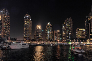 Fototapeta na wymiar Night view from the promenade of Dubai Marina with illuminated skyscrapers, a water channel, yachts and ships in Dubai city, United Arab Emirates
