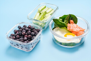 Healthy food in glass lunch boxes on blue background close-up.