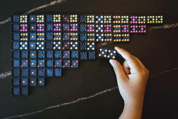 Young girl using her hand to check the total number of dominoes before playing. People search and find missing dominoes. Neatly arranged dominoes. Classic domino tiles on dark table background.