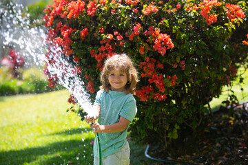 Child playing in garden, pours from the hose, makes a rain. Happy childhood concept.