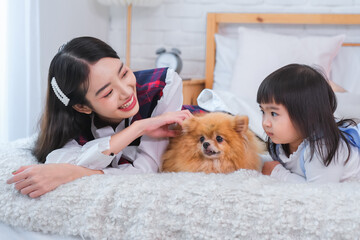 Beautiful asian woman and the little girl were playing with the dog on the bed in the bedroom showing their love for each other.