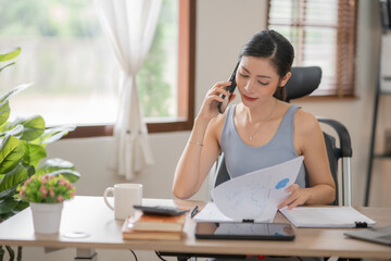 Young Asian businesswoman reading graphs and talking on phone with customers in office