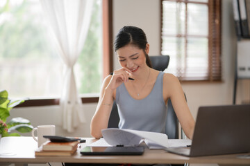 Obraz premium Young Asian businesswoman reading graphs and talking on phone with customers in office