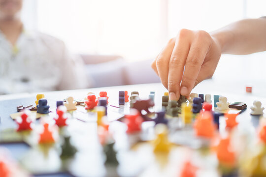 Board game playing concept. People hands hold meeple figures for playing board game on board game field with many figure, dice, models at home. Playing game with friends, family, child on holiday trip
