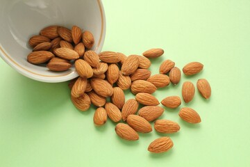 Almond on white ceramic bowl on green background. Healthy eating diet, nutrition, vegan concept. Protein organic food. Dry snack. National nut day. Copy space for text