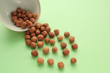 Hazelnut on white ceramic bowl on green background. Healthy eating diet, nutrition, vegan concept. Protein organic food. Dry snack. National nut day. Copy space for text