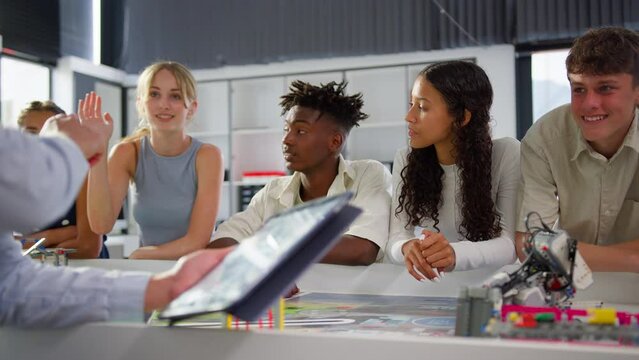Close up of female teacher with digital tablet teaching high school student STEM class as female student raises hand to ask question  - shot in slow motion