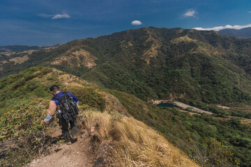 Hiker man with backpack walking along the edge of a hill on a hot sunny day in the province of Puntarenas in Costa Rica