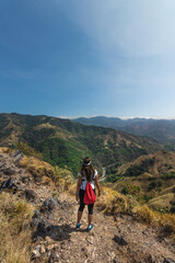Fototapeta na wymiar young hiker woman with red backpack contemplating the landscape of green mountains full of nature and countryside on a hot sunny day in the province of Puntarenas in Costa Rica