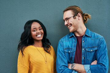 Love, portrait and happy couple laughing against a wall background, bonding and having fun. Interracial relationship, smile and african woman with man outdoors relax and enjoying date or conversation