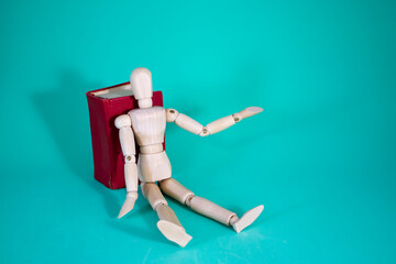 Wood Man and Book. Wooden Figure Sitting. Cheerful Wooden Doll on a Blue Background with a Book. Reading Books Shows Learning. Education concept.