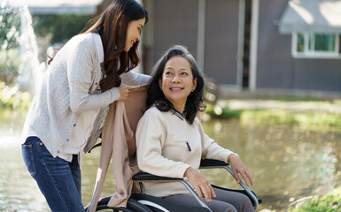 Asian senior woman in wheelchair with happy daughter. Family relationship retired woman sitting on wheelchair in the park age care at retirement home.