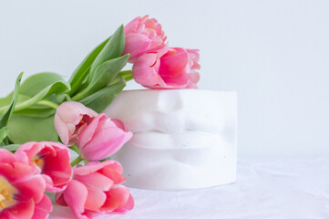 Pink tulips bouquet and plaster statue of lips lying on white wrinkled blanket background copy space