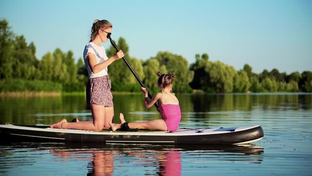 Mother with daughter floating on sup board . Summer family fun
